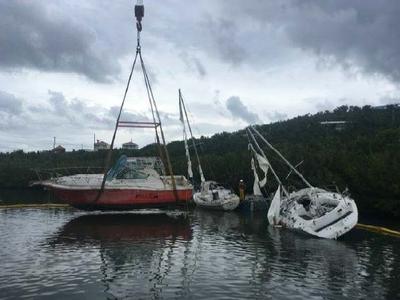 A boat is lifted in a sling beside a sailing vessel lifting to her port